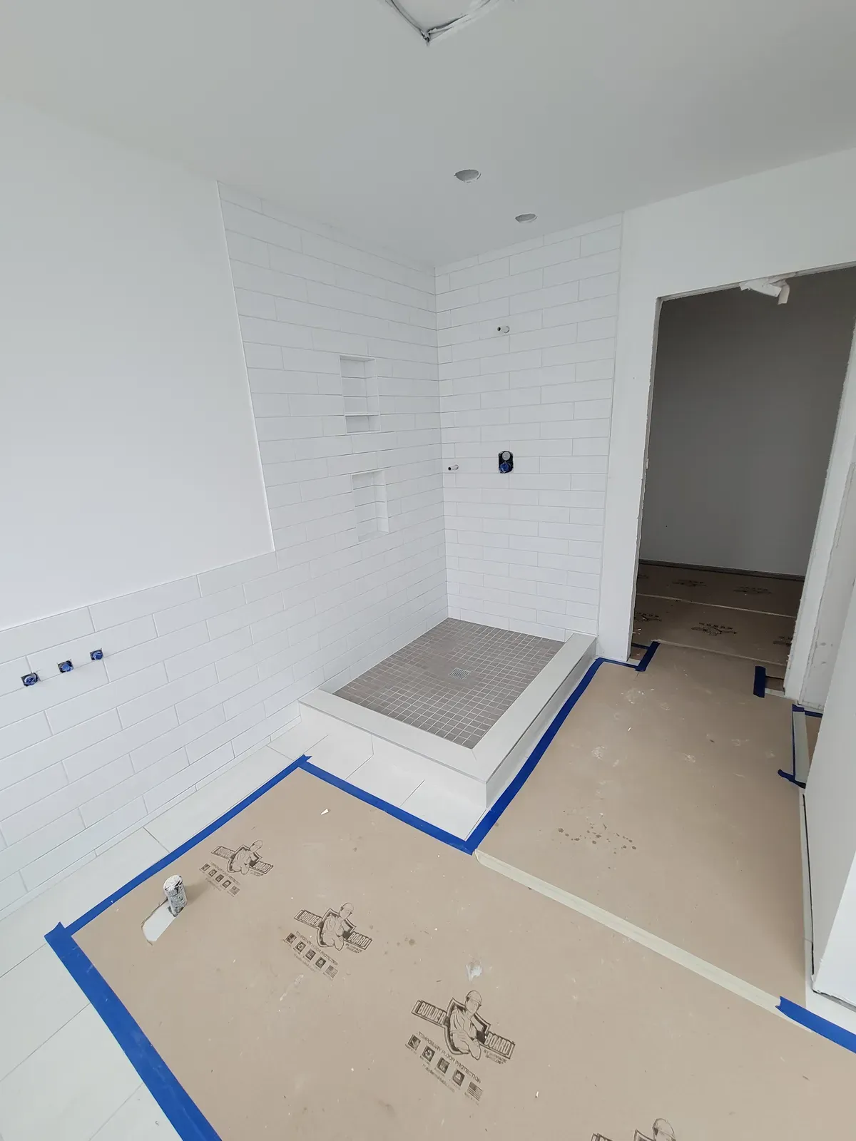 bathroom mid-build: wall tile set, floor protected, valves roughed in