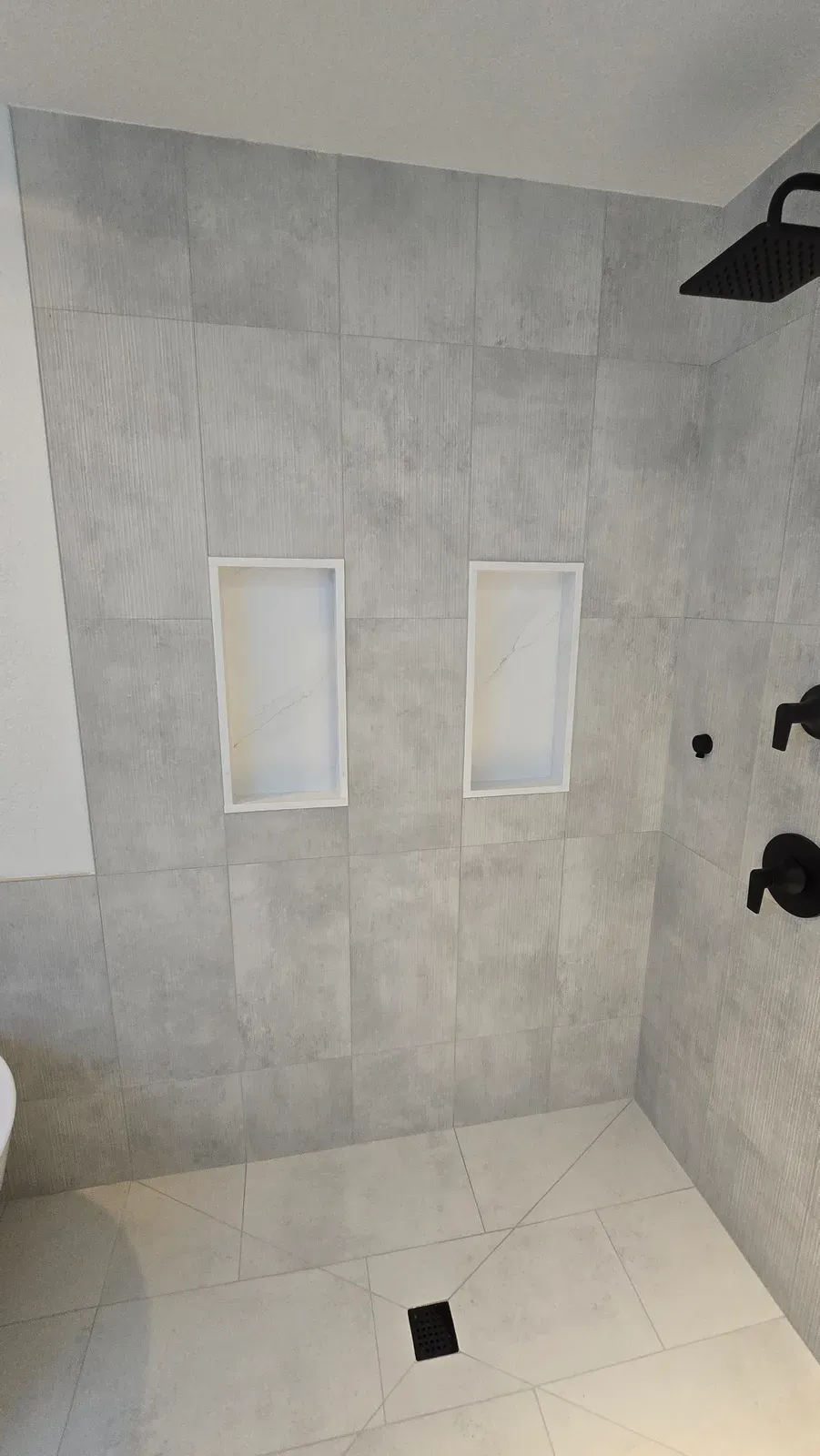 curbless shower with large-format tile, two niches and matte black fixtures