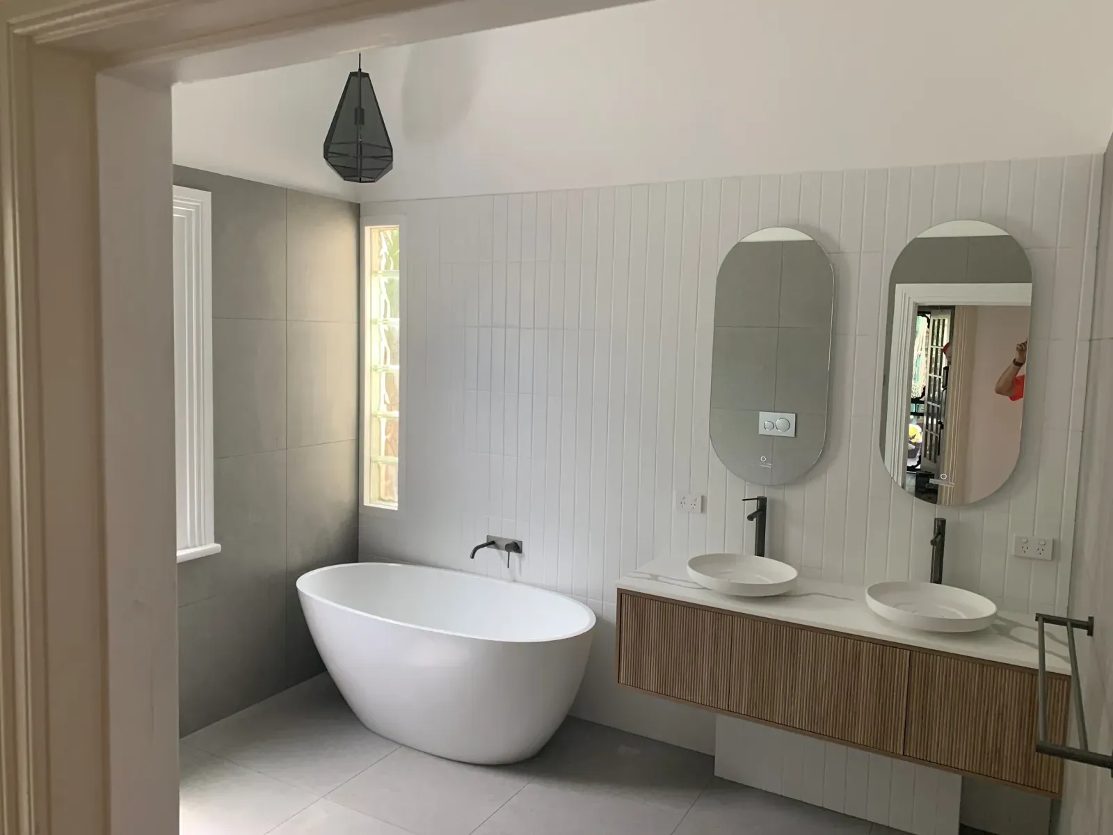 freestanding tub, double vanity and oval mirrors in white vertical tile