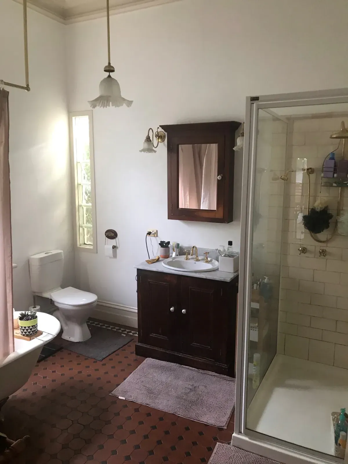 the same bathroom before: dated vanity, small shower and worn floor