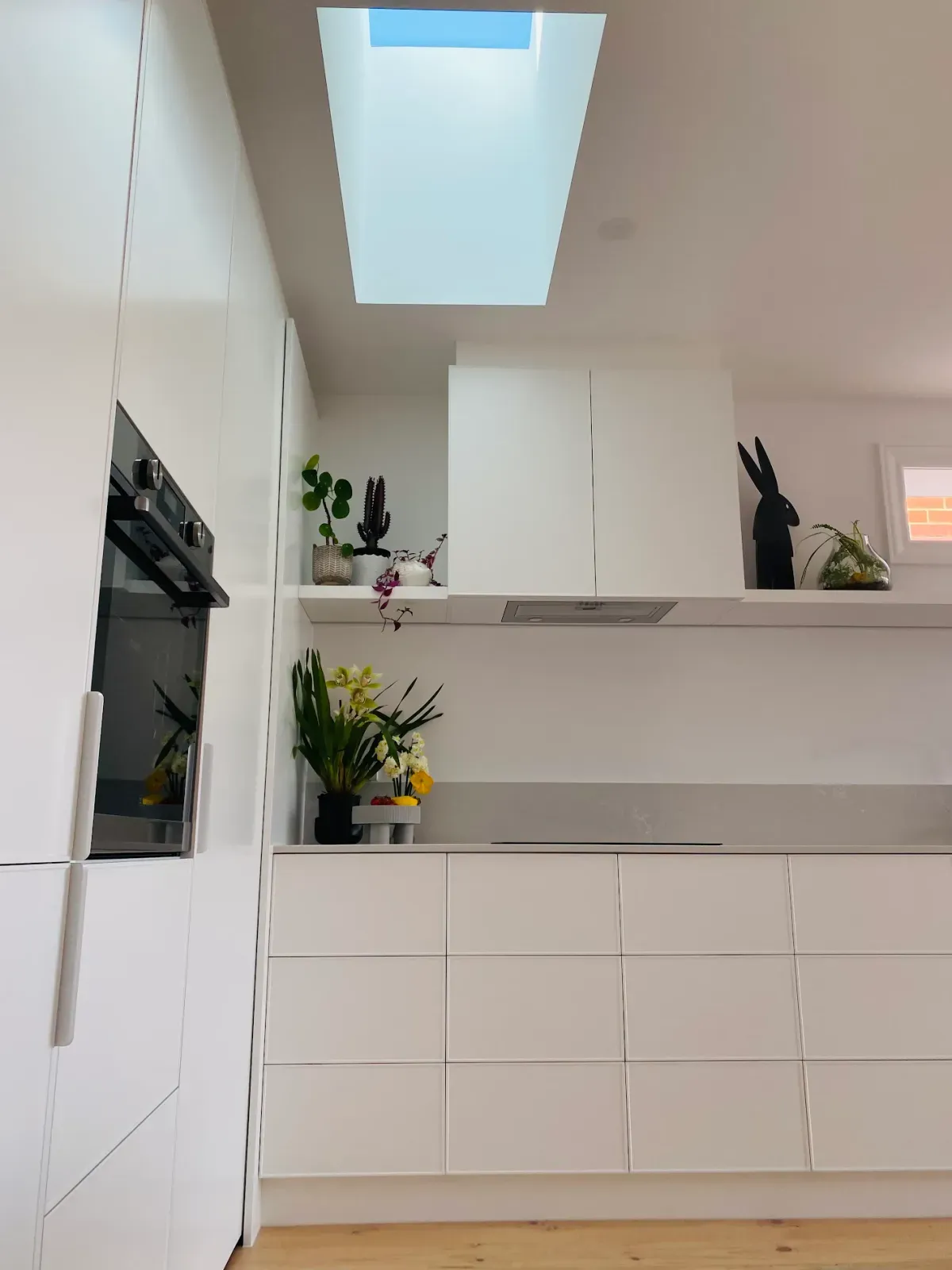 handleless white kitchen with a wall oven under a skylight