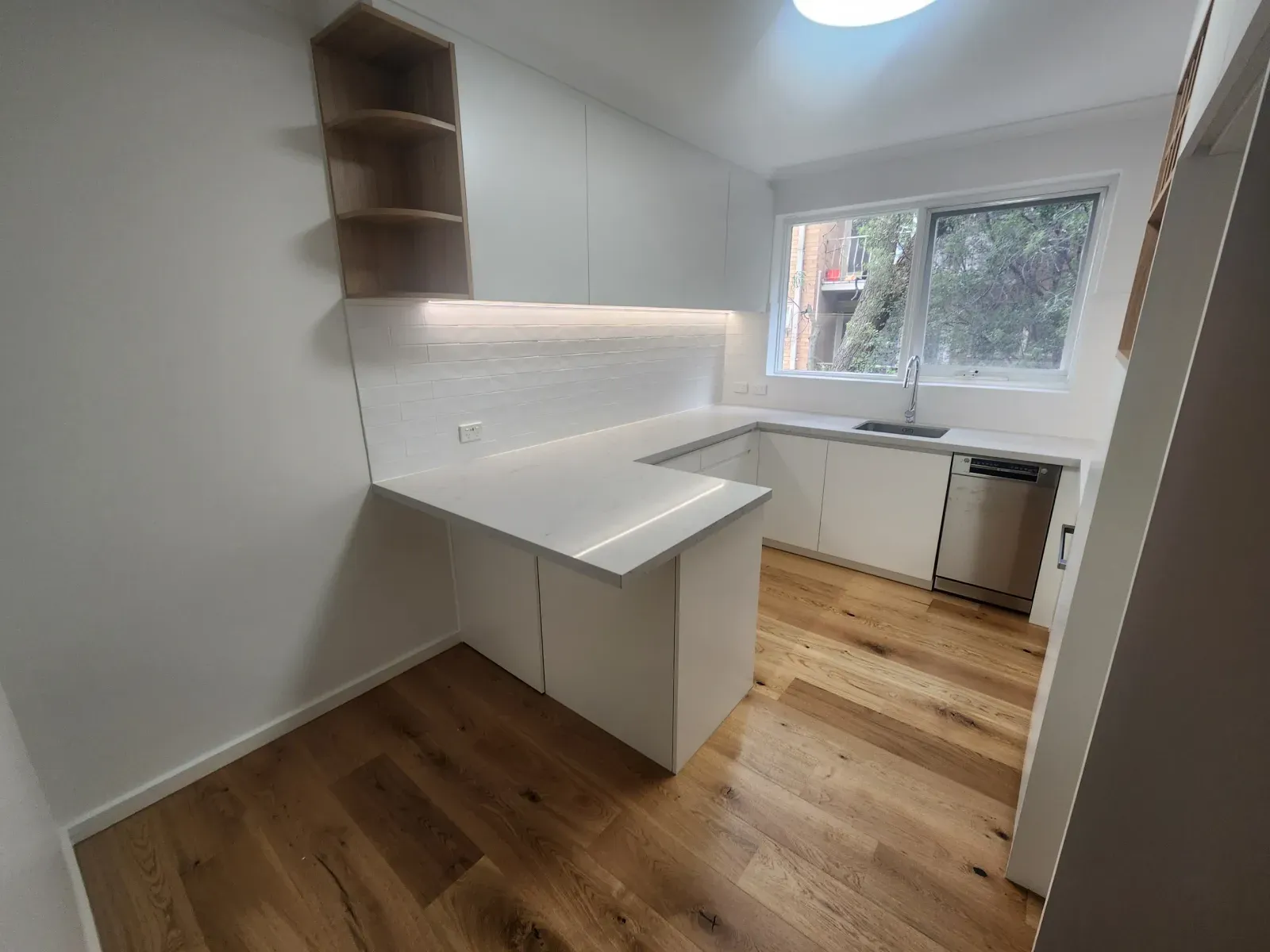 the same kitchen from the dining side: peninsula, open shelves and wood floor