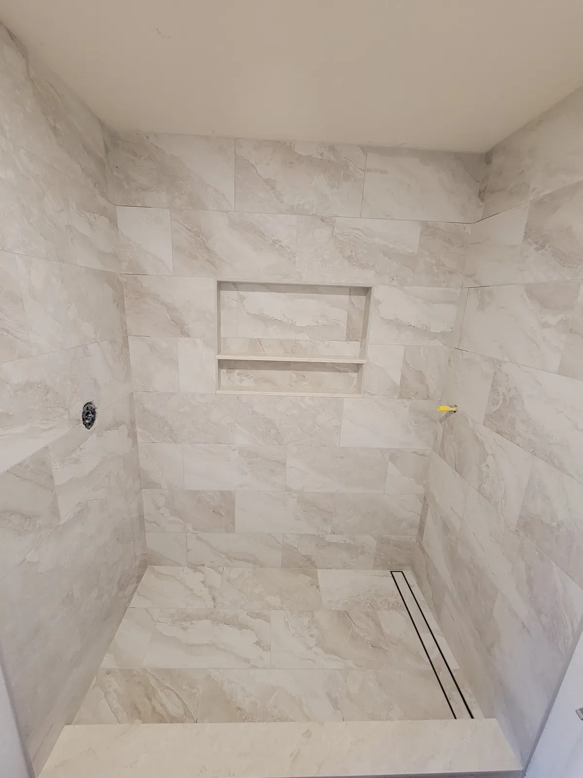shower in marble-look tile with a linear drain and recessed niche, before trim