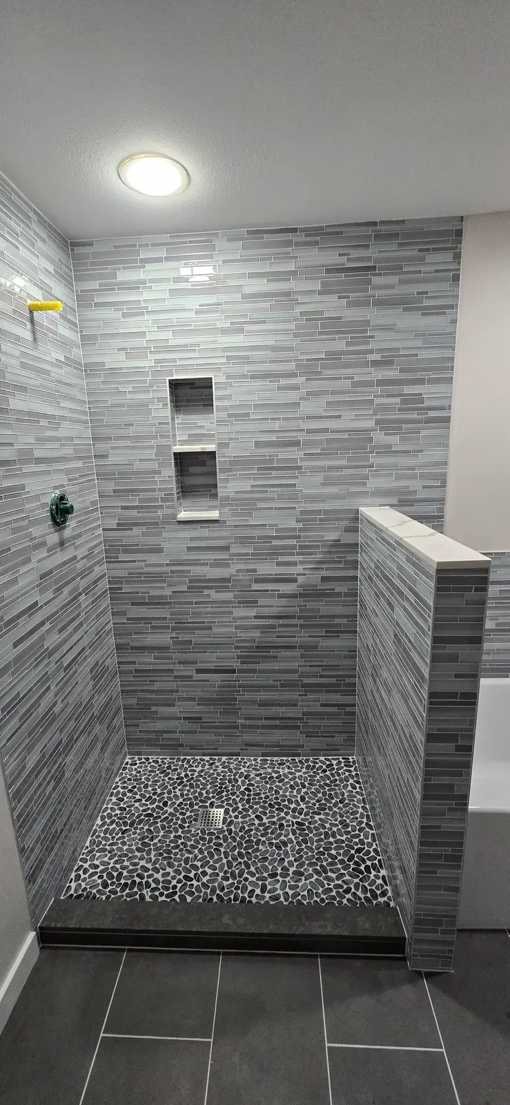 walk-in shower with linear glass tile, pebble floor, double niche and half wall