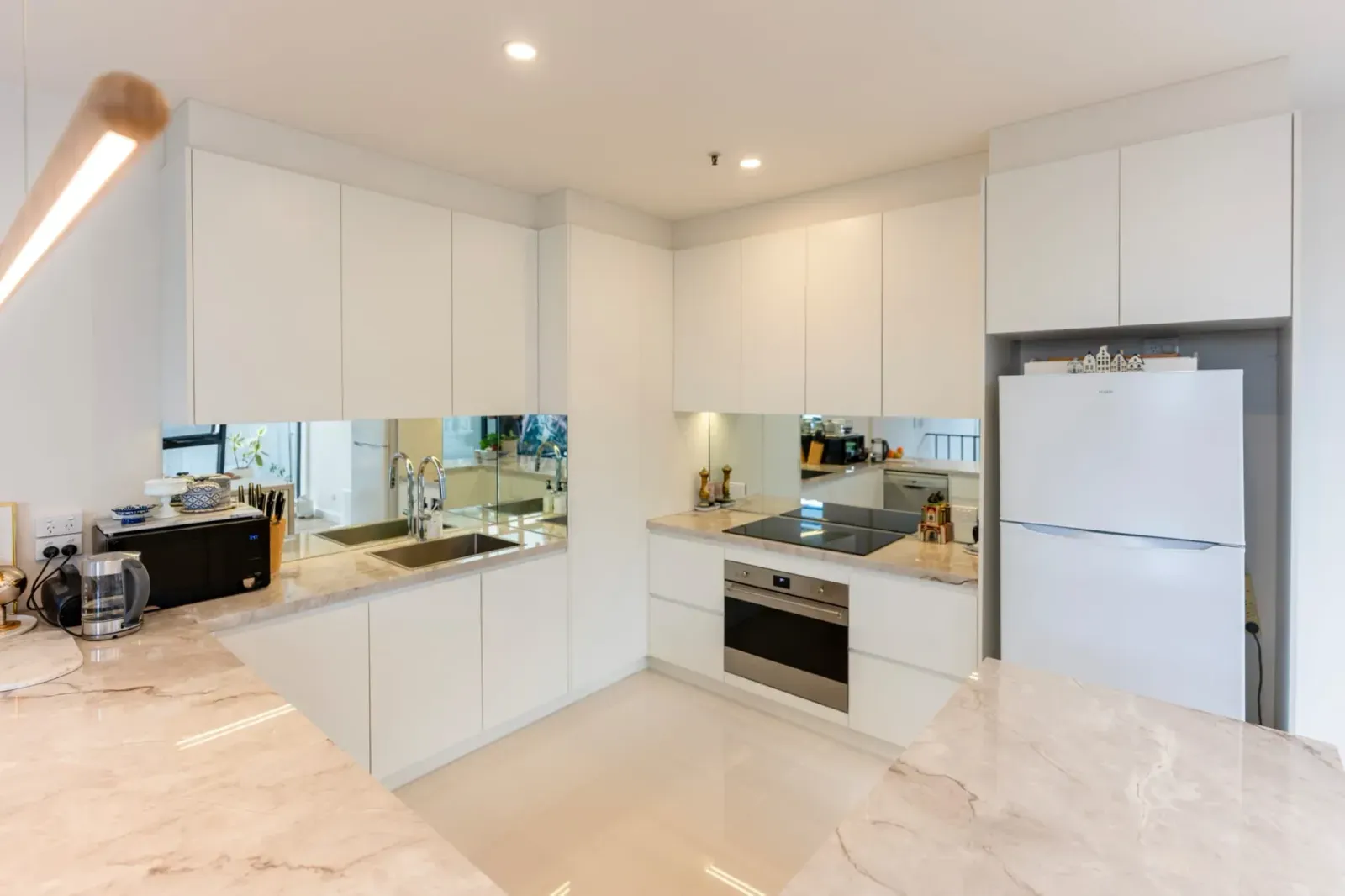 white flat-panel kitchen with marble-look counters and a mirror backsplash